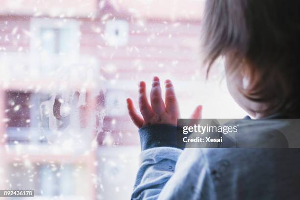 little boy looking out of the window on a snowy day - orphan child stock pictures, royalty-free photos & images