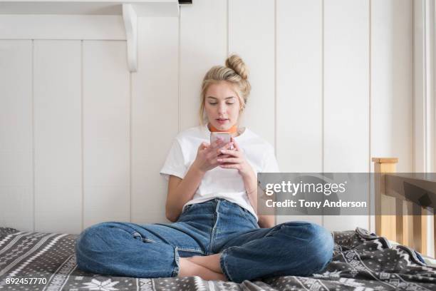 teen girl with phone sitting on bed - woman wearing white jeans stock-fotos und bilder