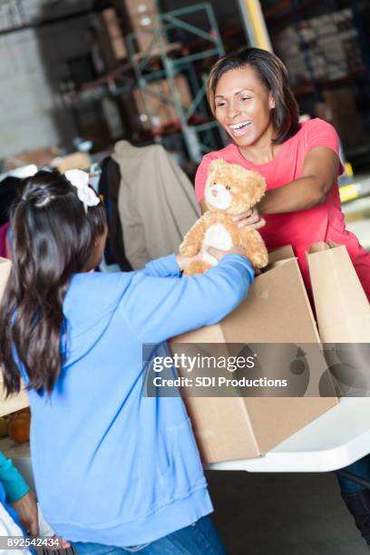 recolha de roupa alegre voluntária dá garota um ursinho de pelúcia - toy drive - fotografias e filmes do acervo