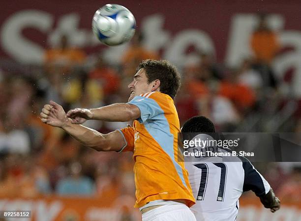 Bobby Boswell of the Houston Dynamo heads the ball away from Kheli Dube of the New England Revolution at Robertson Stadium on July 25, 2009 in...