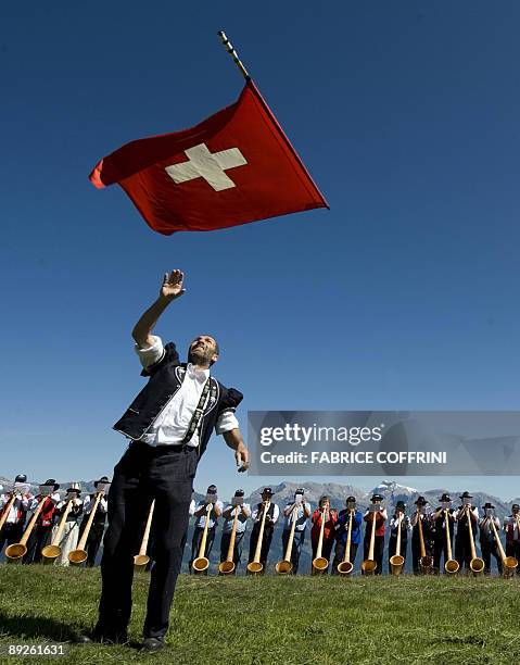 Men throws a Swiss flag as the 120 Alphorn blowers perform all together on the final day of the 6th International Alphorn contest, on the mountain...