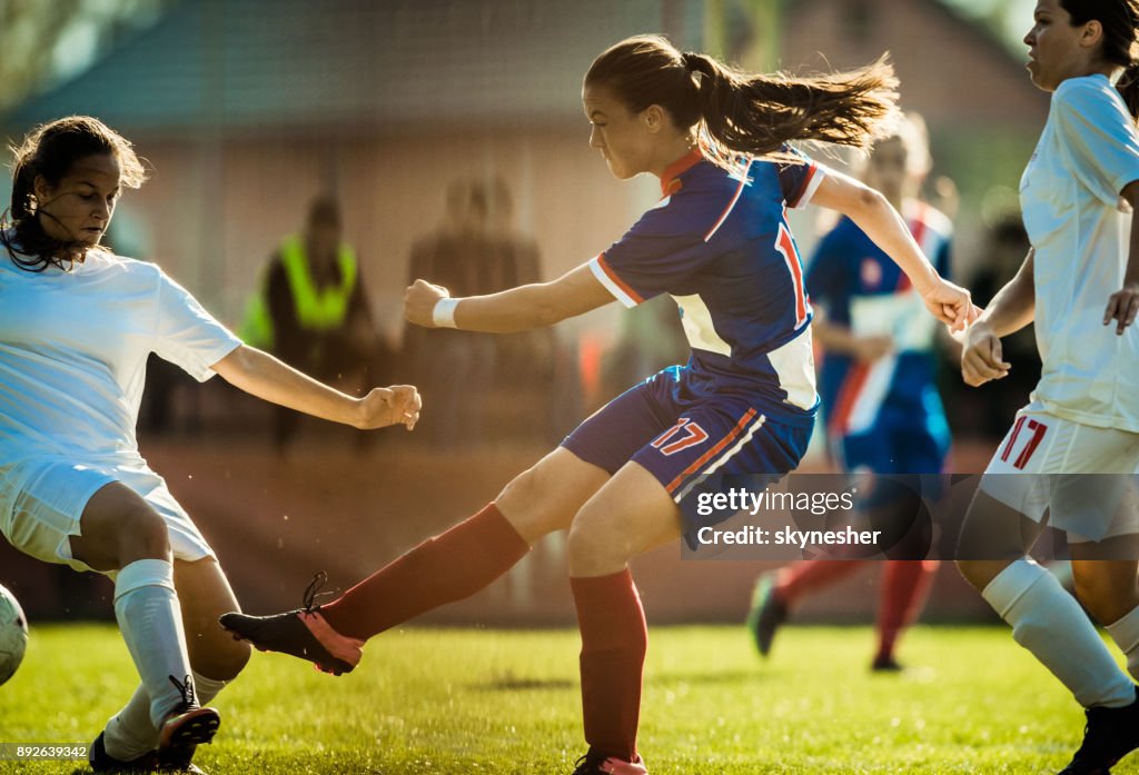 Determined soccer player kicking the ball among rival players on a match.