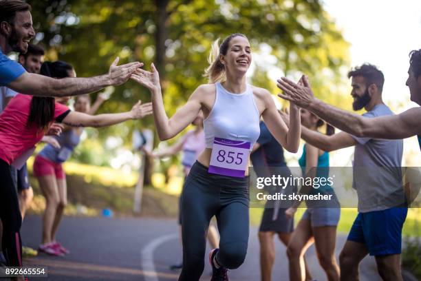 young woman finishing marathon race and greeting with group of supporters. - finishing race stock pictures, royalty-free photos & images