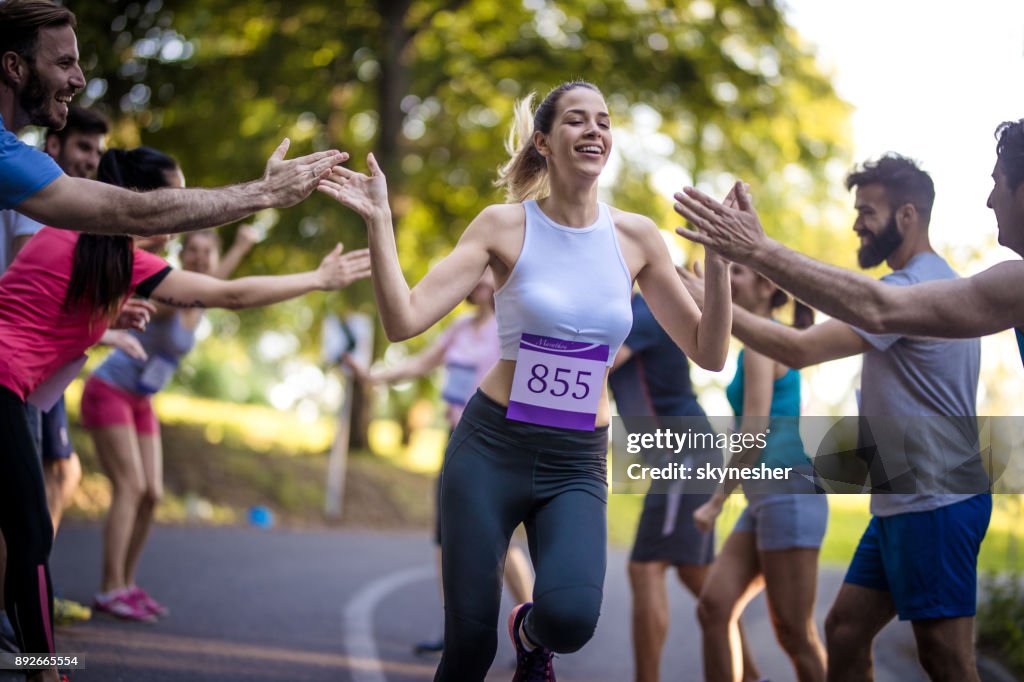 Jovem mulher terminar corrida maratona e cumprimentando com grupo de apoiantes.