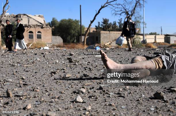 People walk near a body of a prisoner after he was killed in airstrikes targeted the prison on December 13, 2017 in Sana’a, Yemen. More than 12...