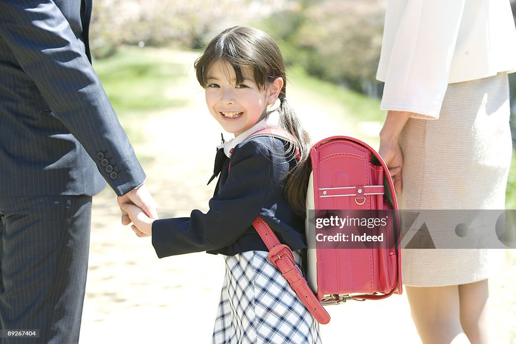 Girl (8-9) smiling, holding hands with parents