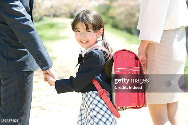 girl (8-9) smiling, holding hands with parents - enfant cartable photos et images de collection