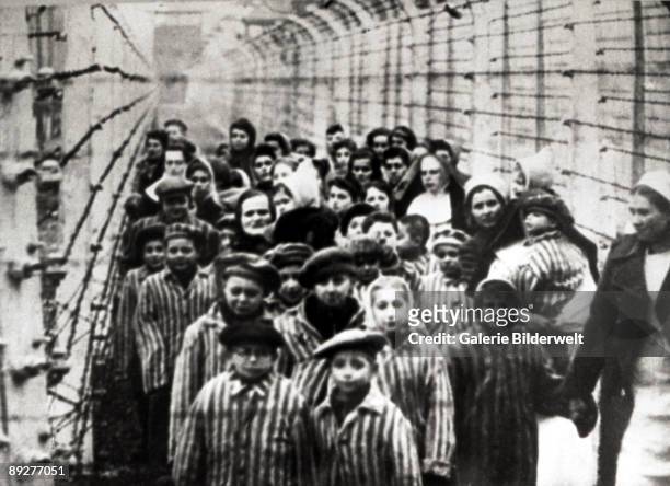 Jewish children, survivors of Auschwitz, with a nurse behind a barbed wire fence, Poland, February 1945. Photo taken by a Russian photographer during...
