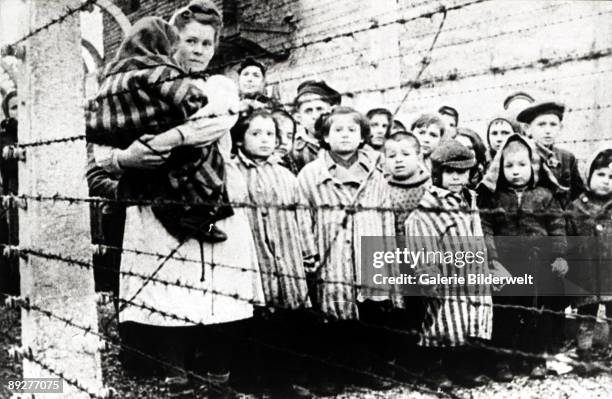 Jewish children, survivors of Auschwitz, with a nurse behind a barbed wire fence, Poland, February 1945. Photo taken by a Russian photographer during...