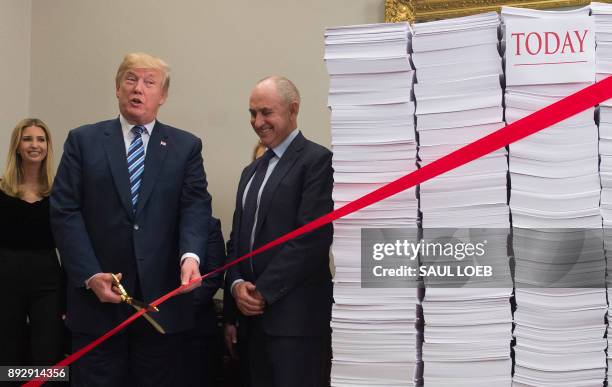 President Donald Trump holds gold scissors as he prepares to cut a red tape tied between two stacks of papers representing the government regulations...