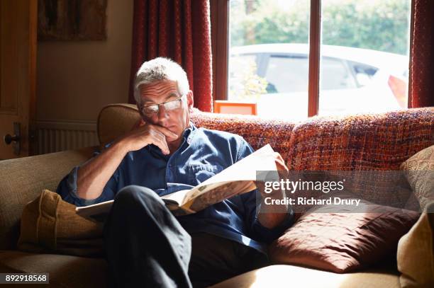 man sitting on sofa reading newspaper - newspapers uk stock-fotos und bilder