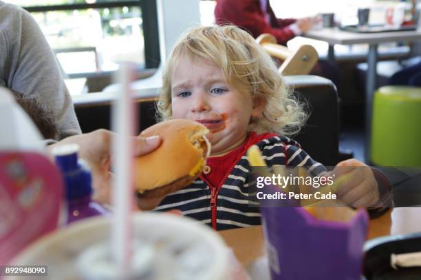 upset toddler being given burger in fast food restaurant - kid eating burger bildbanksfoton och bilder