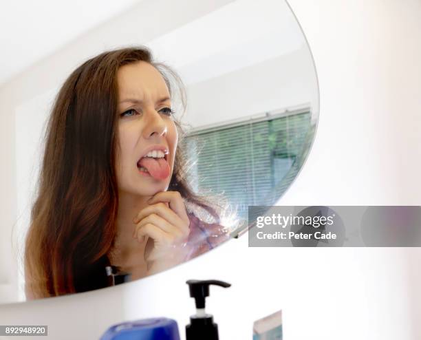 woman looking at her tongue in bathroom mirror - human tongue foto e immagini stock