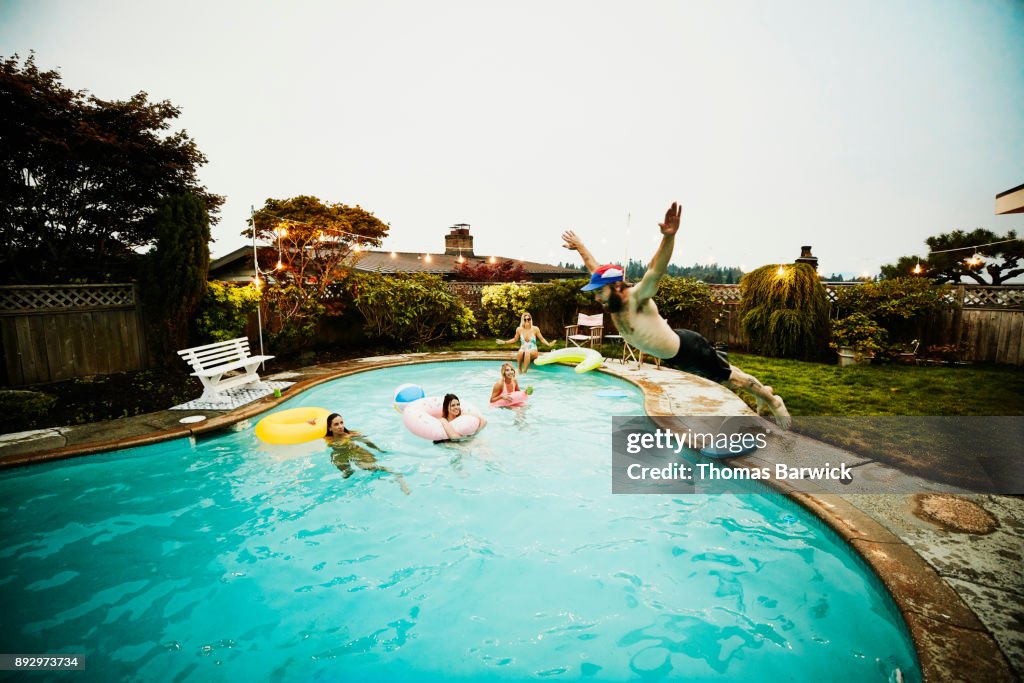 Man doing belly flop into backyard pool during party with friends on summer evening