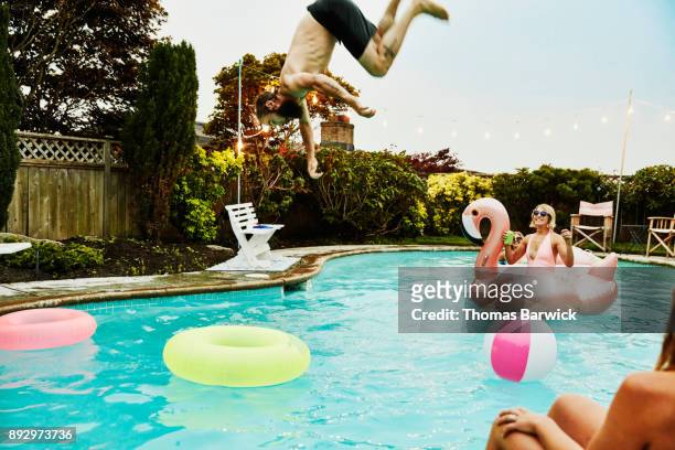man flipping into backyard pool while friends watch during party on summer evening - poolparty bildbanksfoton och bilder