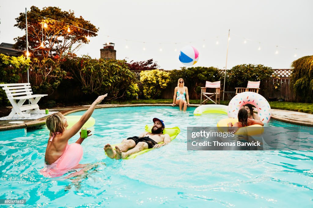 Smiling friends playing in backyard pool during party on summer evening