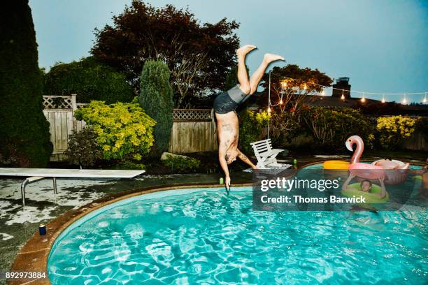 man doing backflip into pool while friends watch during party on summer evening - jump in pool stockfoto's en -beelden