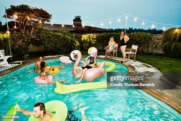 smiling and laughing group of friends having backyard pool party on summer evening - pool party stock pictures, royalty-free photos & images