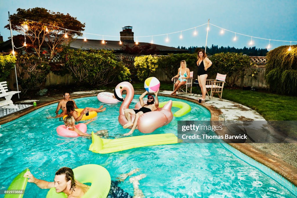 Smiling and laughing group of friends having backyard pool party on summer evening