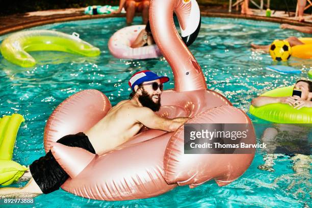 smiling man hanging out on inflatable pool toy during party with friends on summer evening - millennials at party photos et images de collection