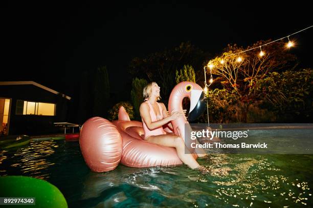 laughing woman riding inflatable pool toy during party with friends on summer evening - kitsch stock-fotos und bilder