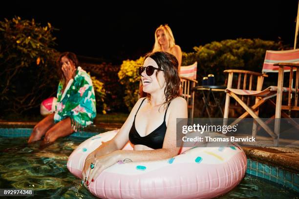 laughing woman standing in inflatable pool toy during backyard pool party with friends on summer evening - pool party night stock pictures, royalty-free photos & images