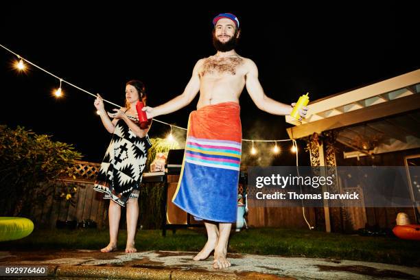 smiling man wrapped in towel holding ketchup and mustard while grilling for friends in backyard during party on summer evening - offbeat fotografías e imágenes de stock