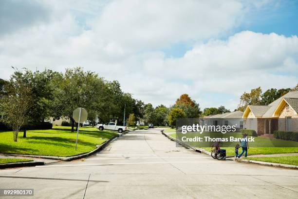 father in wheelchair out for walk with wife and daughter on neighborhood street - area urbana malfamata foto e immagini stock