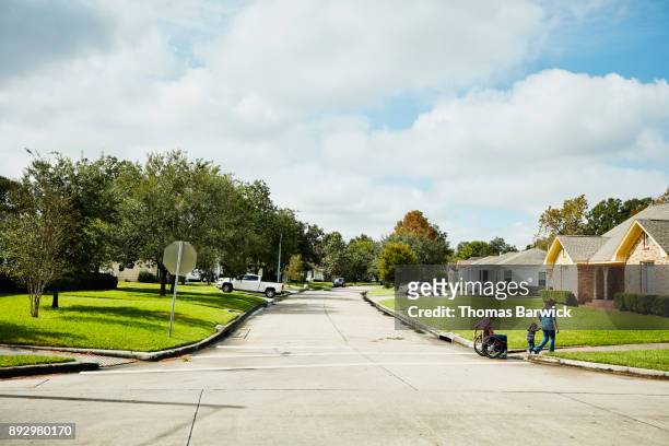 father in wheelchair out for walk with wife and daughter on neighborhood street - street stock pictures, royalty-free photos & images