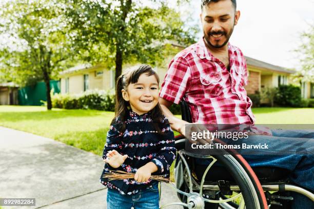 laughing daughter out for walk through neighborhood with father in wheelchair - wheelchair stock pictures, royalty-free photos & images