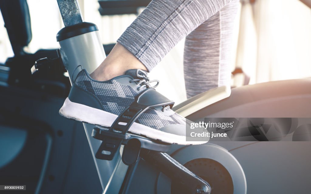 Woman feet is cycling on fitness exercising bike machine