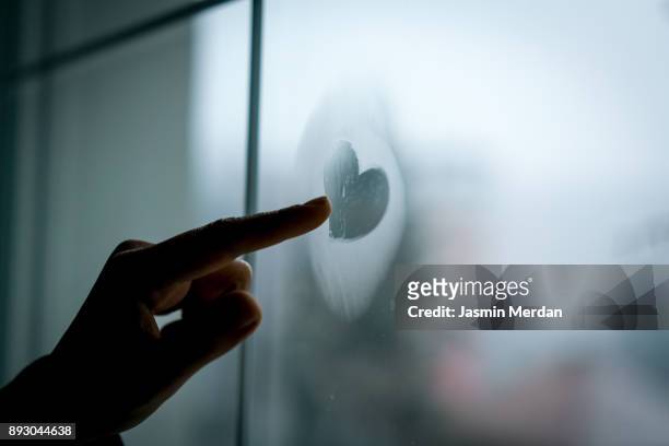 hand drawing heart on winter window glass - freezing hands stock-fotos und bilder