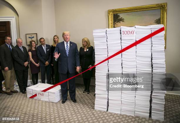 President Donald Trump prepares to cut a red ribbon between two stacks of paper, representing the regulatory code from 1960 compared to today, during...