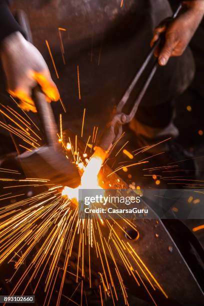 knife maker shaping hot piece of iron on anvil with hammer - fucina foto e immagini stock