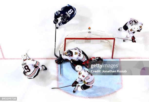 Goaltender Corey Crawford of the Chicago Blackhawks covers up the puck with his glove as Jacob Trouba of the Winnipeg Jets tries to poke it loose...