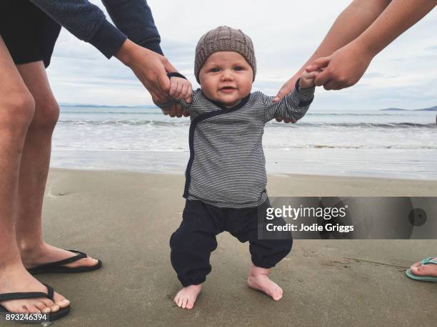 Happy young baby standing outside at the beach with the help of older siblings
