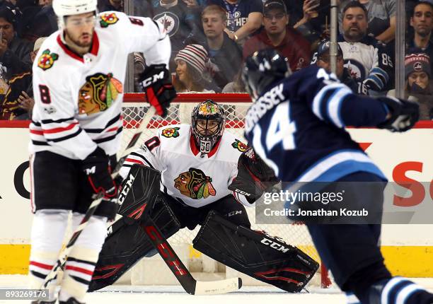 Goaltender Corey Crawford of the Chicago Blackhawks keeps his eye on the puck as Josh Morrissey of the Winnipeg Jets shoots it down the ice during...