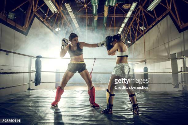 full length of two women dueling on a boxing match in health club. - mixed martial arts stock pictures, royalty-free photos & images