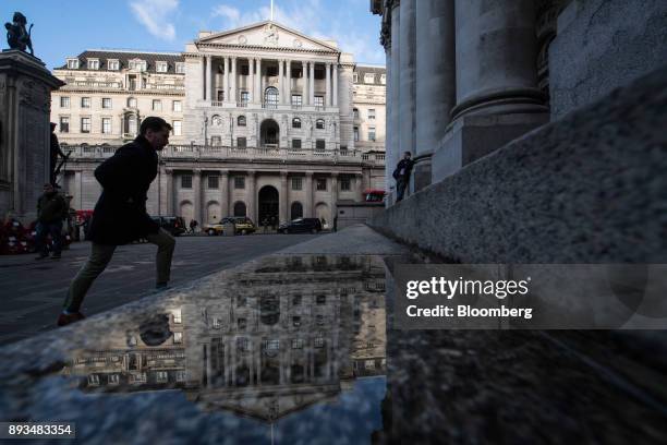 Pedestrian walks over a puddle reflecting the Bank of England in the City of London, U.K., on Friday, Dec. 15, 2017. Bank of England policy makers...