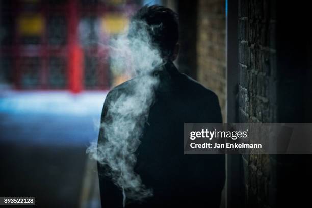 man smoking in a dark alleyway - crime or recreational drug or prison or legal trial fotografías e imágenes de stock