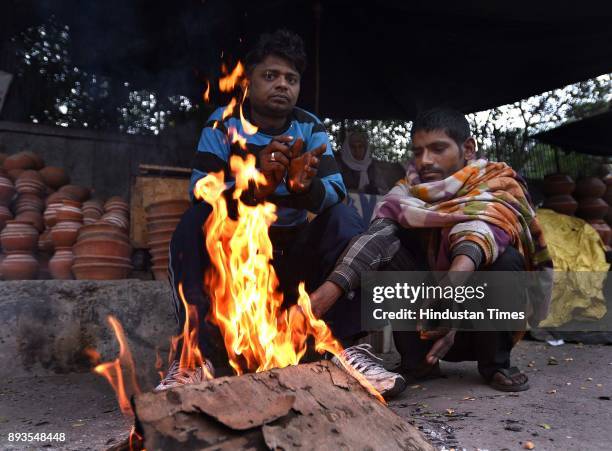 People warm themselves by a bonfire on a cold winter morning, on December 15, 2017 in New Delhi, India. Expect a further dip in temperature as cold...