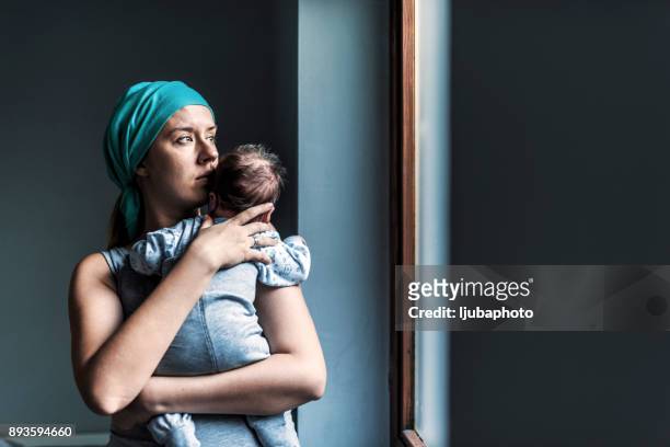 thoughtful woman looking out the window while holding her son - contemplation family imagens e fotografias de stock