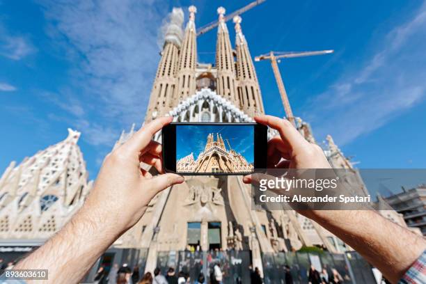 tourist photographing sagrada familia in barcelona with smartphone - sagarda stock pictures, royalty-free photos & images