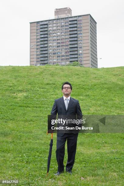 businessman with umbrella standing on grassy knoll - burca fotografías e imágenes de stock