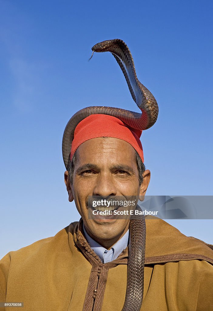 Snake charmer smiles with a Cobra on his head.