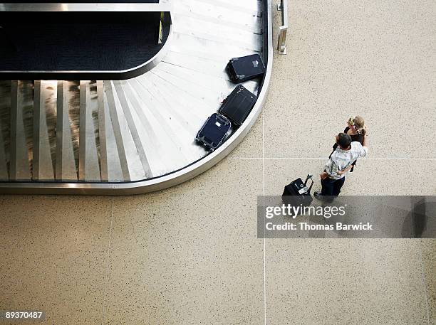 couple waiting for luggage at baggage claim  - airport indoor stockfoto's en -beelden