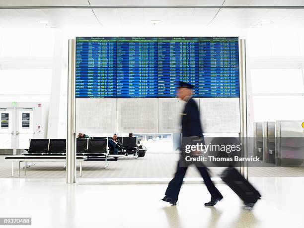pilot with luggage walking past departure board - flight time stock pictures, royalty-free photos & images