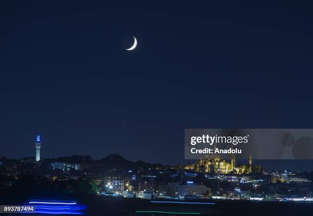 Suleymaniye Mosque and Beyazit Tower at night with crescent moon in the sky in Istanbul, Turkey on August 25, 2017.