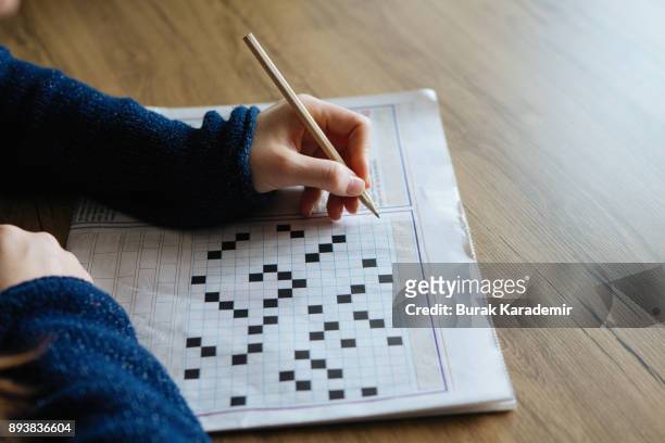 female hand holding a pencil and solves crossword puzzle - kreuzworträtsel stock-fotos und bilder