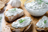 Homemade greek tzatziki sauce in a glass bowl with sliced bread on a wooden board. Close-up, horizontal image, selective focus on bread